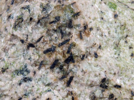 Glassy, nearly black allanite, most 4-7 mm in length on ivory-colored feldspar partly altered to green epidote