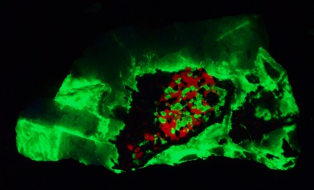 Massive white gypsum cementing altered clasts of granular franklinite-willemite-calcite ore under shortwave UV Light